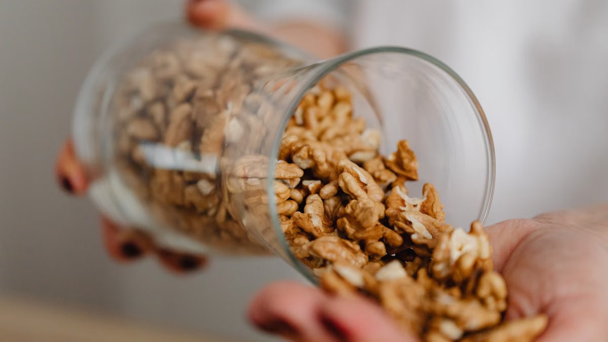 Hands pouring walnuts from a glass jar, featuring a rustic kitchen scene.